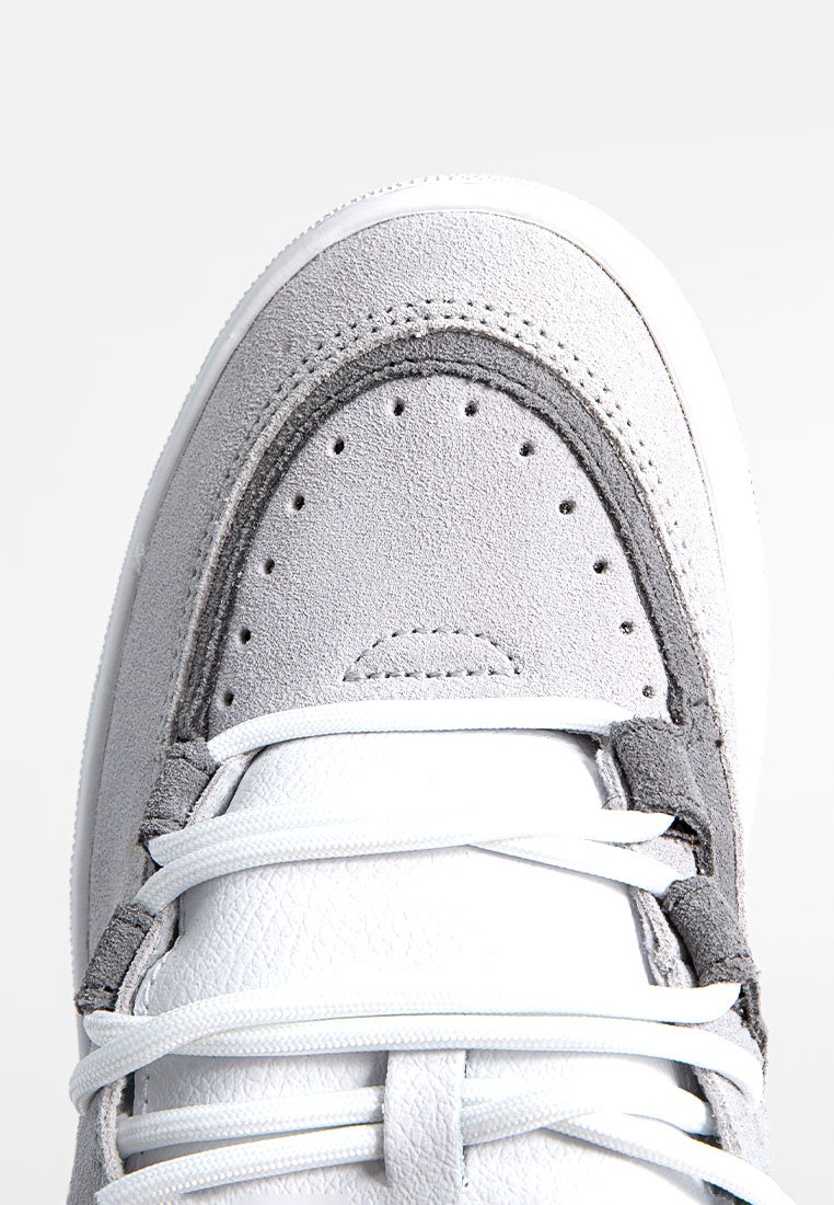 Sneaker bianco con punta in suede grigio texturizzato, superiore in pelle bianca liscia e lacci bianchi piatti. Presenta perforazioni per la traspirabilità.