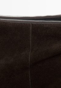 Nahaufnahme von schwarzem Wildlederstoff mit vertikalem Nahtdetail unter einem teilweise sichtbaren silbernen Reißverschluss.