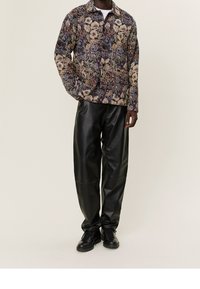 Chaqueta de manga larga con estampado floral en multicolores con cierre de botones, combinada con pantalones de cuero negros de corte holgado y zapatos negros.