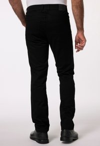 Svarta slim-fit byxor med en slät textur, två bakfickor och en läderetikett på midjan. Bärs med svarta skor, sedd från baksidan.