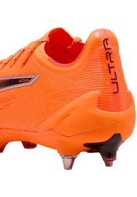 Narancssárga focicipő struktúrált felsőrésszel, fényvisszaverő elemekkel és fekete kiegészítőkkel. Formázott stoplikat tartalmaz a tapadás érdekében gyepszőnyeges felületeken.