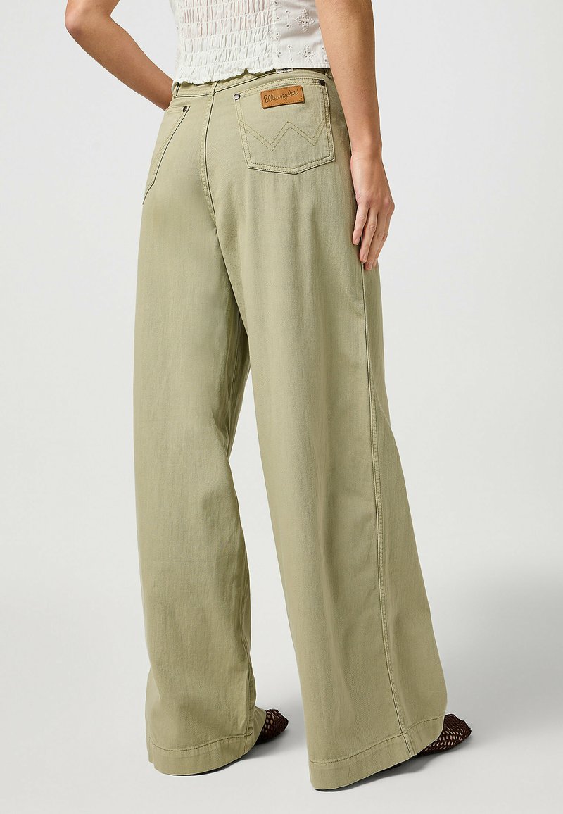 Pantalons larges vert clair en tissu doux, dotés de deux poches arrière et d'une étiquette en cuir avec le logo de la marque sur la taille.