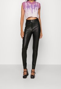 Gilet tricoté court en rose clair avec un motif de gouttes violettes ; pantalon noir en cuir synthétique taille haute ; chaussures à talons épais noires.