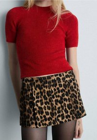 Haut rouge à manches courtes en tricot, associé à une mini-jupe à imprimé léopard avec des plis et une texture lisse. Des collants noirs complètent la tenue.