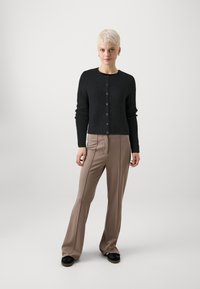 Μαύρο, υφασμένο καρδιόν με κουμπιά, σε συνδυασμό με καφέ, φαρδιά παντελόνια που έχουν κεντρικές ραφές και λείο φινίρισμα.