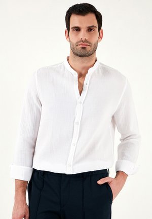 Witte, gestructureerde blouse met een kleine kraag en opgerolde mouwen, gecombineerd met marineblauwe broek. De stof lijkt licht en casual.