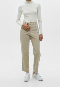 Beige corduroy broek met een hoge taille, rechte pijpen en subtiele ribbeltextuur, gecombineerd met een witte ribbel turtleneck en witte sneakers.