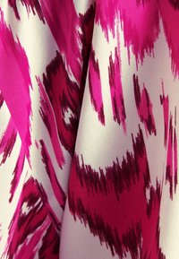 Textil med ett djärvt rosa och vitt abstrakt mönster. Slät textur, med varierande nyanser av magenta och inslag av djupa röda accenter.