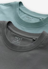 Två crew-neck t-shirts, en i ljus teal och den andra i mörkgrå, med ribbade kragar och etiketter som anger storlek och märke.