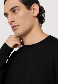 Czarna koszula z długim rękawem wykonana z miękkiego materiału, z okrągłym dekoltem i subtelnym logo na piersi. Gładka struktura, dopasowany krój.