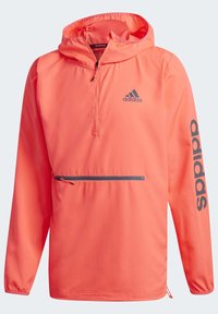 Korallinvärinen huppumallinen tuulenpitävä takki, jossa on neljännesvetoketju, etutasku, jossa on tummansininen vetoketju, ja tummansinisellä "adidas"-logolla vasemmassa hihassa.