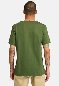 Zelené tričko vyrobené z měkké tkaniny, s kulatým výstřihem, krátkými rukávy a rovně střiženým lemem. Jednoduchý design bez viditelných vzorů.