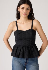 Svart peplum-top med blomsterbroderi, justerbare stropper, tettsittende overdel og utsvingt bunn. Båret over blå denimjeans.