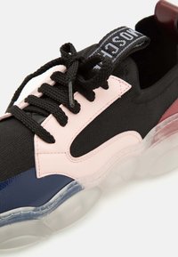 Basket noire avec des accents roses et bleu marine, semelle épaisse transparente, lacets noirs attachés en nœud et languette brandée sur la langue.