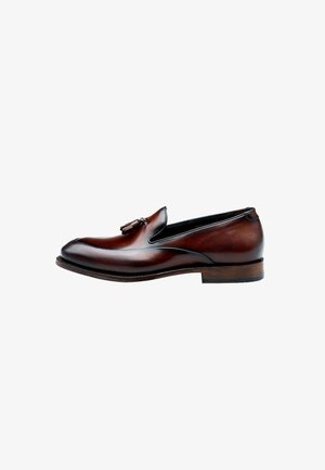 Brown leather slip-on shoe with tassel detail, rounded toe, tonal stitching, and a low wooden heel. Smooth texture with polished finish.