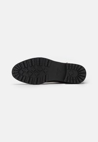 Suela de bota de goma negra con patrones de tracción profundos y forma redondeada, con el nombre de la marca grabado a lo largo del lateral.