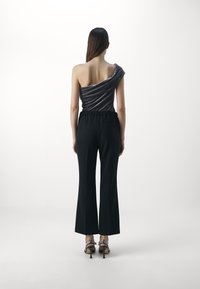 Celana panjang lebar hitam dipadukan dengan atasan abu-abu satu bahu yang memiliki bahan draped. Pakaian ini dilengkapi dengan sandal bertumit tinggi.