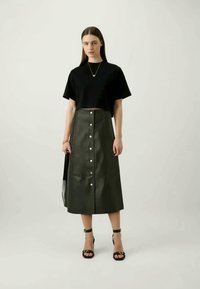 Black cropped t-shirt paired with a dark green button-down midi skirt made of a smooth material. The outfit includes black strappy sandals.