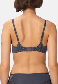 Tummansininen rintaliivi, jossa on pitsiyksityiskohtia takana. Säädettävät olkaimet ja useita hakaset, jotka sulkeutuvat koukku-kilven avulla. Silkkinen pinta.