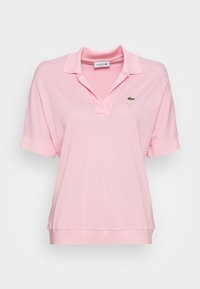Różowa bawełniana koszulka polo o luźnym kroju, krótki rękaw, żebrowany kołnierzyk oraz wyszywane na zielono logo Lacoste na piersi.