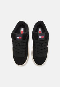 Svart semsket sneakers med rund tå, tykke svarte lisser og en hvit gummisåle. Har et tri-farge logo-merke på tungen.