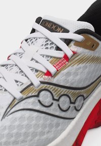 Λευκό αθλητικό παπούτσι με μαύρο και χρυσό σχέδιο, λευκά κορδόνια, κόκκινα ραφτά διακοσμητικά, μαύρο περιλαίμιο στη φτέρνα και ετικέτα "LONDON" στη γλώσσα.