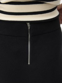 Juoda sijonas su lygiu paviršiumi, turintis sidabrinę užtrauktuko detalę juosmenyje, derinamas su juodu ir kreminės spalvos dryžuotu viršumi.