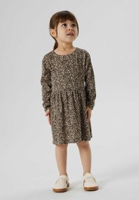 Langdrogende jurk met een beige en bruine gevlekte print, voorzien van een getailleerde taille en een uitlopende rok. Gepaarde met crèmekleurige schoenen.