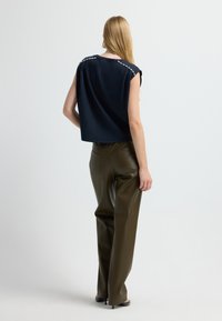 Marineblaues Cropped-Top mit kurzen Ärmeln und verzierten Schultern. Kombiniert mit dunkelolivgrünen Lederhosen und offenen High Heels.