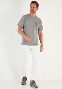 Siva kratka majica s teksturiranim žepom na prsima, u kombinaciji s uskim bijelim trapericama i sivim sportskim cipelama. Jednostavan dizajn, ležeran izgled.