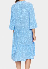 Blå klänning med polka prickar och trekvarts, klockformade ärmar. Har en flerlagers kjol och rundhals. Tillverkad av lättviktig tyg.