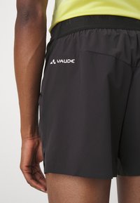 Pantalones cortos vaude negros con cintura elástica, bolsillos laterales y un logo en el muslo izquierdo. Textura ligera y suave, y longitud por encima de la rodilla.