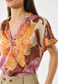 Kortærmet bluse i livlig blomsterprint med orange, pink og brune nuancer. Letvægtsstof med en afslappet pasform og V-udskæring.