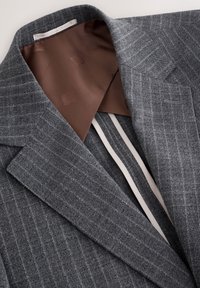 Blazer gris à fines rayures avec doublure marron à motif et larges revers, présenté à plat avec col ouvert.
