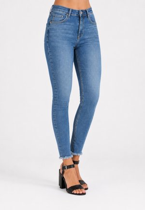 Vaqueros ajustados azules con dobladillos deshilachados, combinados con sandalias negras de tacón alto con tiras en el tobillo y hebillas.