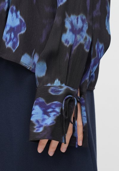 Μαύρη μπλούζα με μπλε λουλουδάτο σχέδιο, υφασμάτινη με υφή, μακριά μανίκια και δεμένα μανσόνια. Διαθέτει στρωματοποιημένο, ρέον σχέδιο.