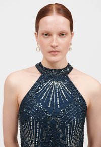 Abito halter in navy con complessi lavori di perline e paillettes, caratterizzato da un colletto superiore e motivi geometrici dettagliati su tutta la stoffa.