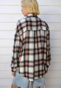 Geruit oversized shirt in zwart, wit en roest. Kenmerkt zich door een button-down kraag en lange mouwen, met een langere achterkant en een zachte textuur.