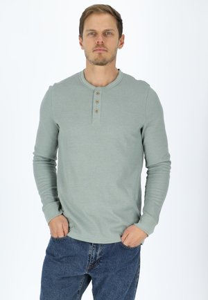 Long-sleeve henley shirt in soft, mint green fabric with a round neckline, three wooden buttons, and ribbed cuffs. Worn with blue jeans.