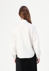 Biela, ľahká blúzka s dlhými, nadýchanými rukávmi a zaobleným lemom. Má klasický golier a čistý, minimalistický dizajn.