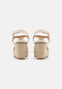 Sandalias de plataforma beige con tacones de cuerda trenzada, correas en el tobillo ajustables y una plantilla texturizada. La vista trasera muestra un intrincado diseño de correas.