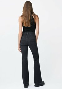 Jean en denim noir évasé avec une taille haute, doté de deux poches arrière et d'une texture sombre et lisse. Porté avec un débardeur noir ajusté.