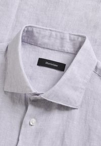 Col de chemise en lin violet clair avec un bouton blanc fermé et une étiquette noire portant l'inscription « Matinique » à l'intérieur de l'encolure.