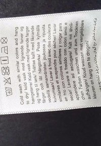 Mosási útmutató címke több nyelven és szabványos mosási jelekkel fehér anyagon.