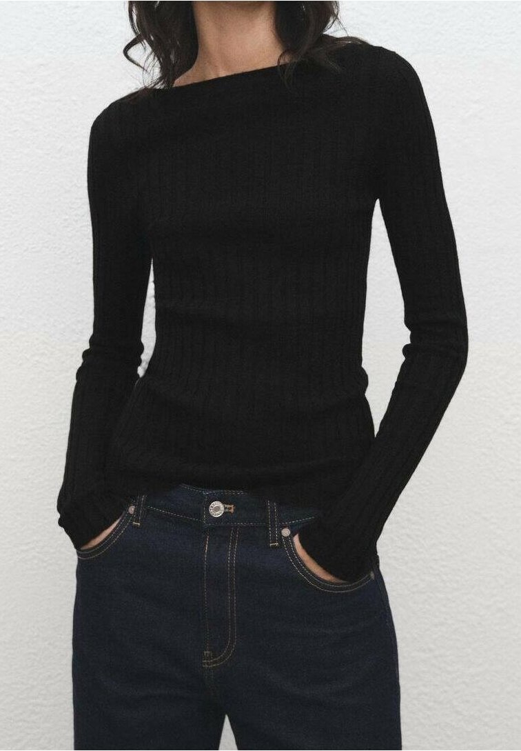 Femme portant un haut côtelé noir ajusté à manches longues, rentré dans un jean bleu foncé taille haute, les mains dans les poches.
