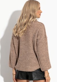 Jasnobrązowy sweter dziany o prążkowanej fakturze, w luźnym fasonie i z rękawami 3/4. Dół jest nieco dłuższy z tyłu.