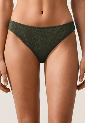 Femme portant un bas de bikini taille haute vert foncé avec motif léopard texturé.