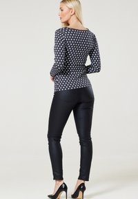 Langärmliges Oberteil in Dunkelgrau mit weißem Sternmuster, kombiniert mit schwarzen glänzenden Leggings und schwarzen High-Heels.