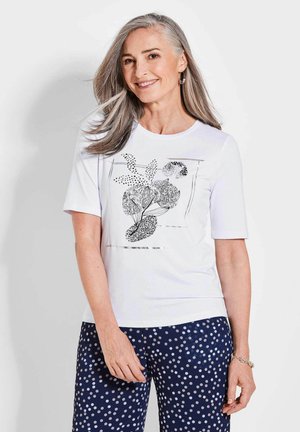 White short-sleeve t-shirt featuring a botanical black and silver graphic. Paired with navy pants adorned with white polka dots.