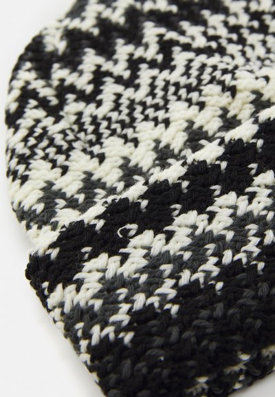 Fekete, fehér és szürke kötött anyag, amelyet houndstooth minta díszít, fehér felületen összegöndörítve.
